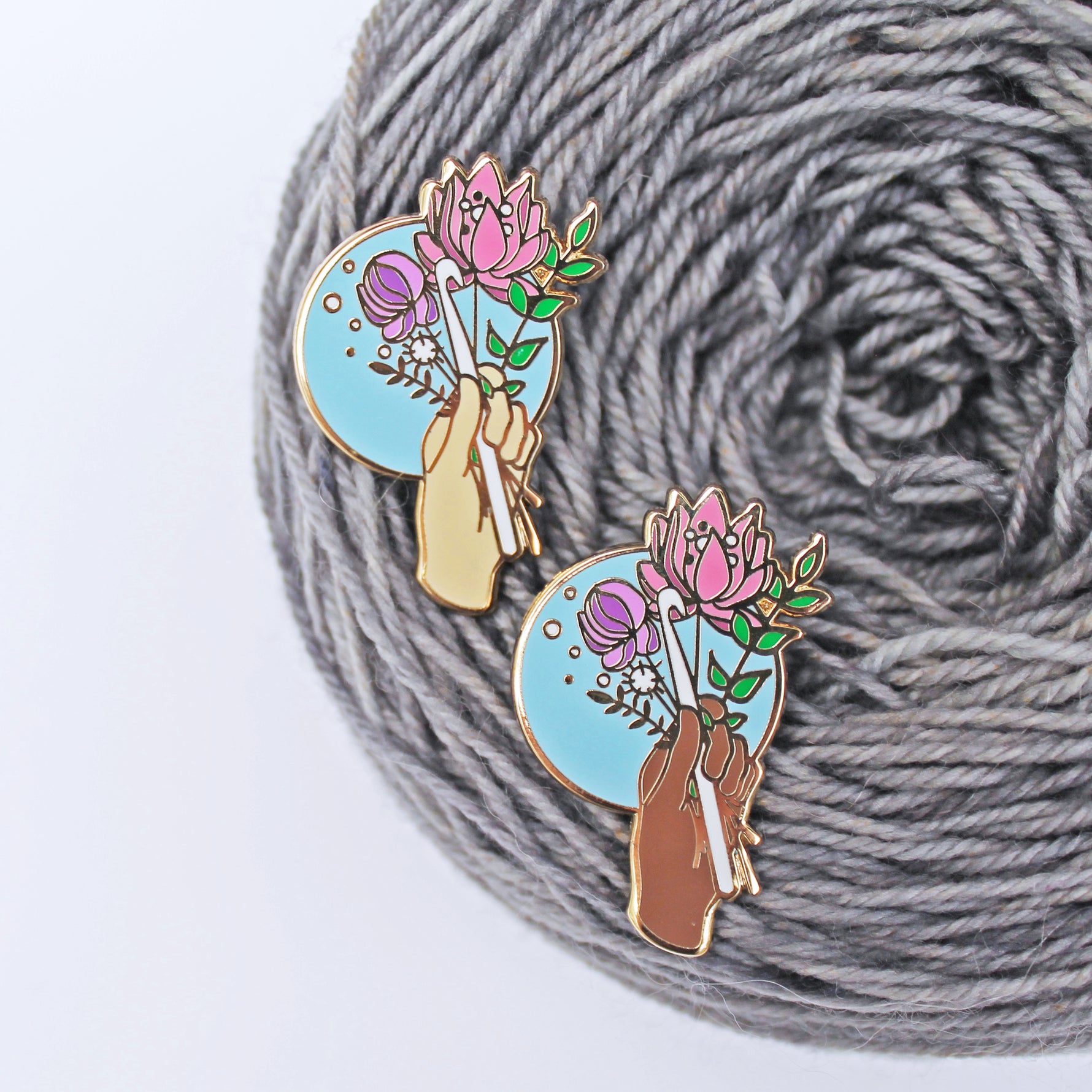 Floral enamel pin for crocheters. A crochet hook being held with a bouquet of flowers, available in multiple skin tones.