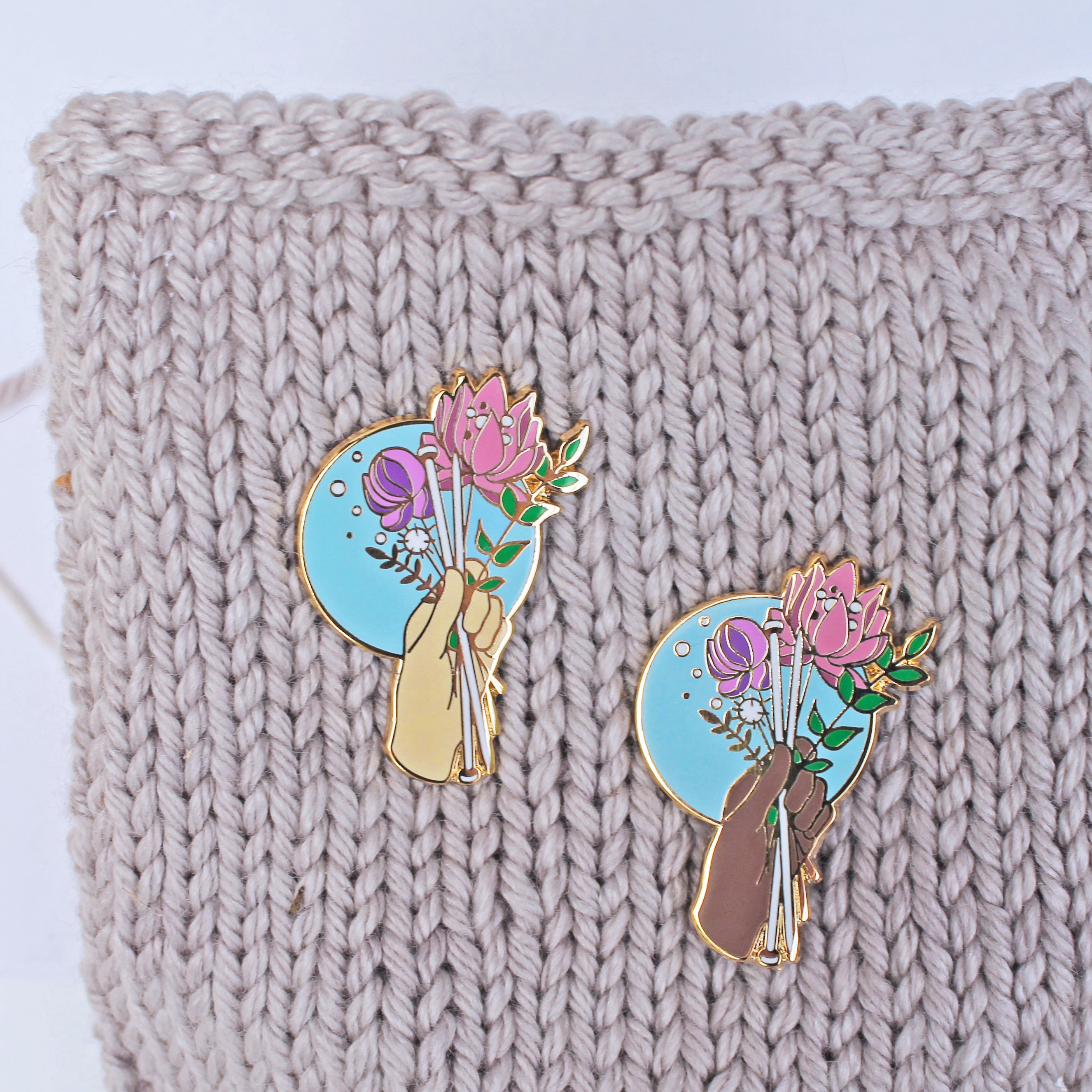 Floral enamel pin for knitters. Knitting needles being held with a bouquet of flowers, available in multiple skin tones.