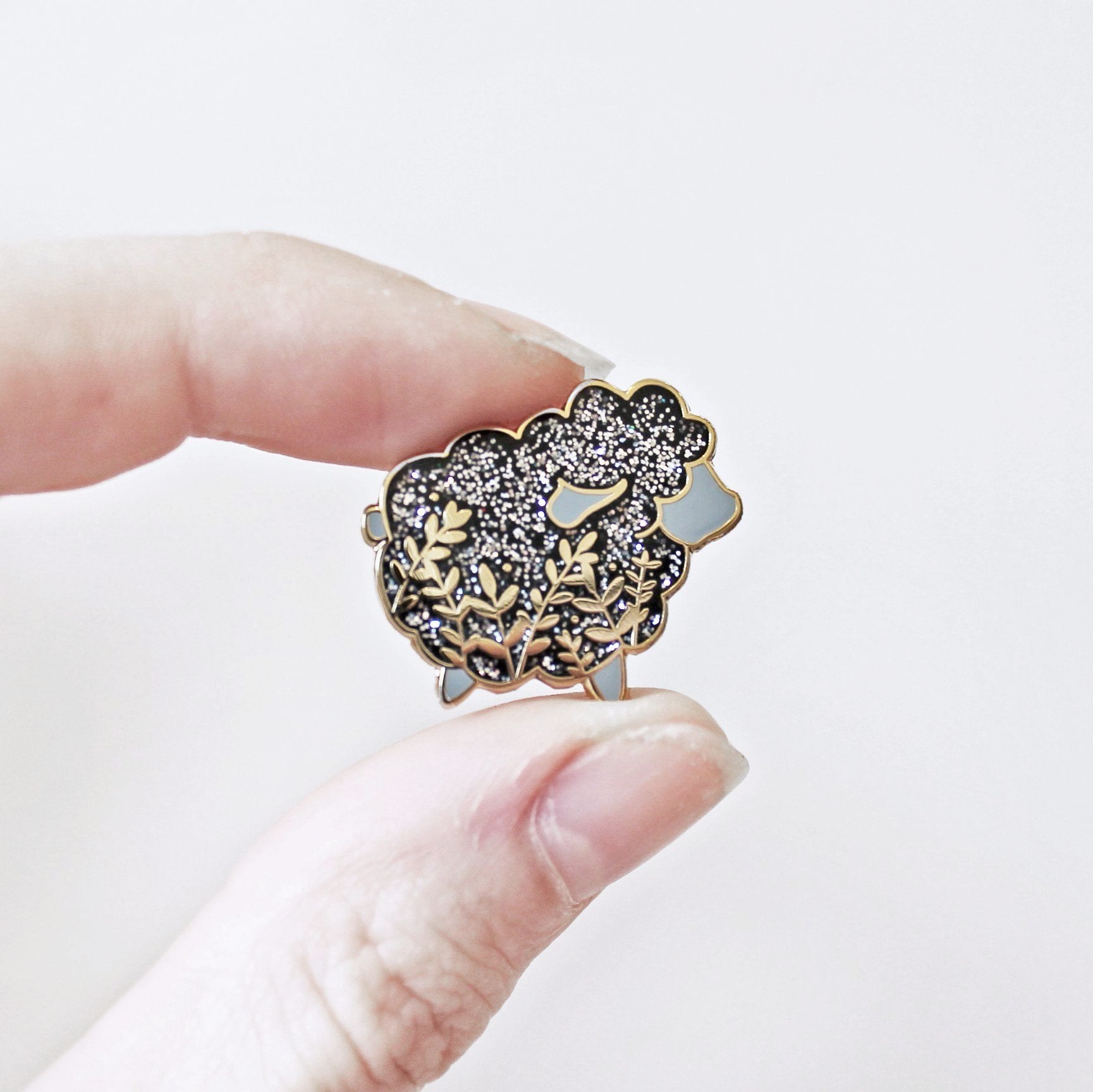 Cute sheep enamel pin with a little floral whimsy and glitter. A beautiful pin made for animal lovers, fiber enthusiasts, knitters and crocheters.