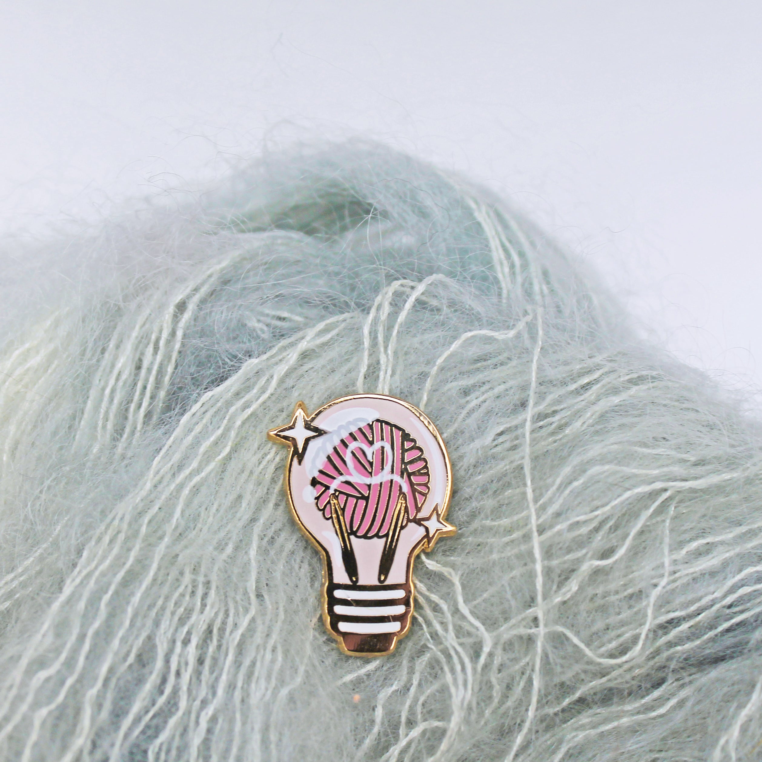 Whimsical and unique enamel pin for knitters. Yarn ball and knitting needles displayed inside a lightbulb.