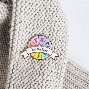 Unique spinning enamel pin for knitters. 'Just One More Row' pin with activity options on spinning pastel rainbow wheel.